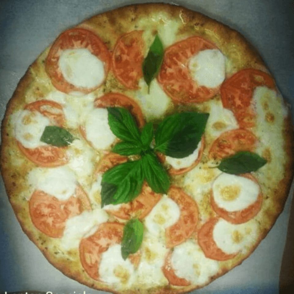 A Pizza Roma Margherita pizza, topped with fresh mozzarella, sliced tomatoes, and basil leaves.