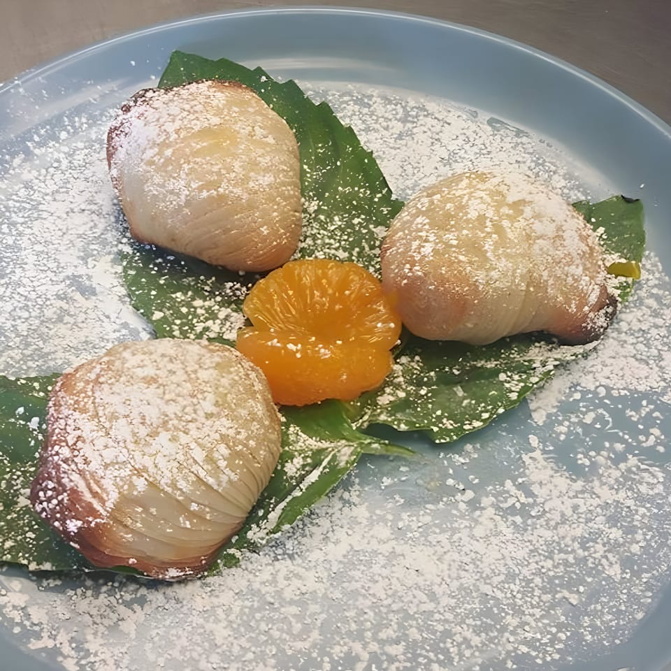 Three powdered sugar-dusted pastries and an orange segment on green leaves, on a blue plate.