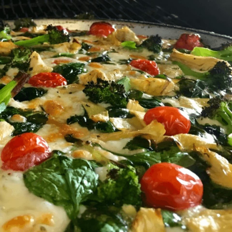 Close-up of a Pizza Roma pizza with melted cheese, cherry tomatoes, broccoli, and spinach.