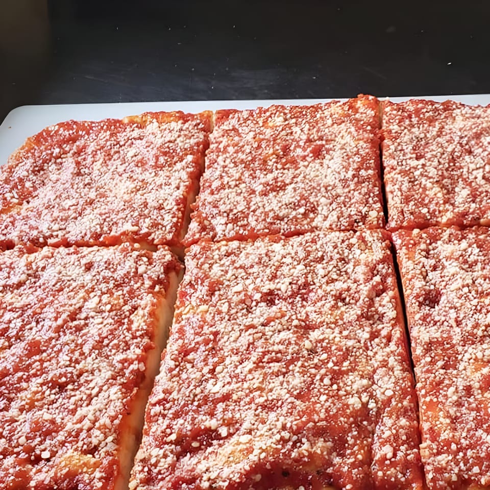 Close-up of a freshly baked square Pizza Roma pizza, cut into six slices, topped with red sauce and cheese.